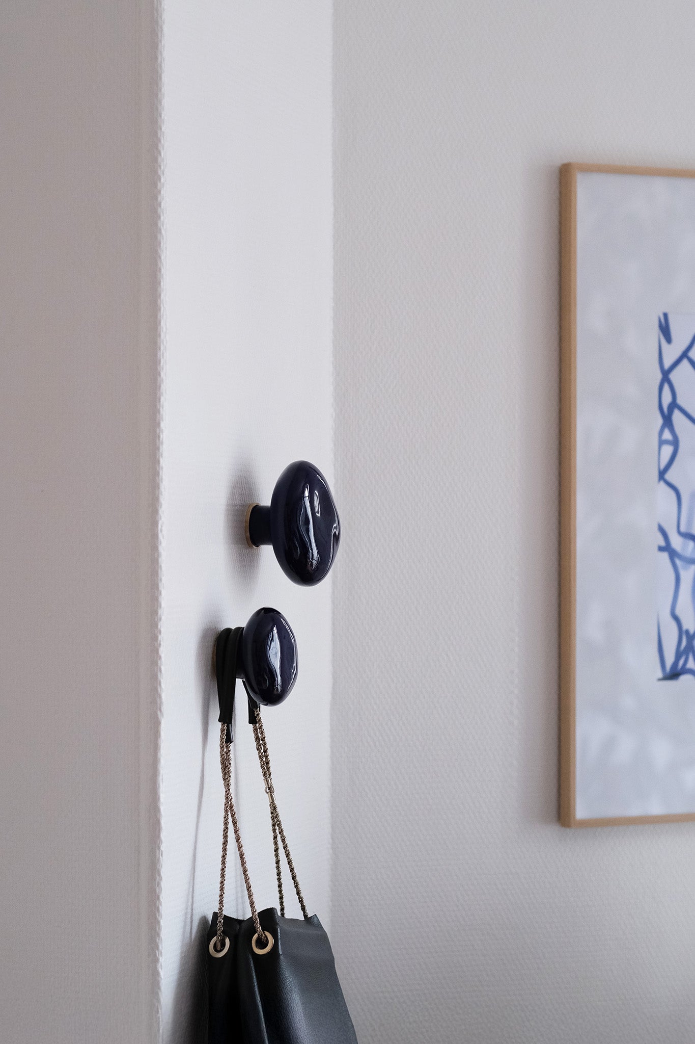 Patères en porcelaine couleur bleu sèvres accrochées au mur d'un appartement moderne et minimaliste. Sac suspendu.