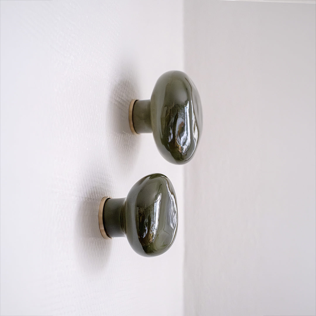 Deux patères Agate vert mousse en porcelaine émaillée, installées sur un mur blanc - vue en gros plan  #couleur_vert mousse
