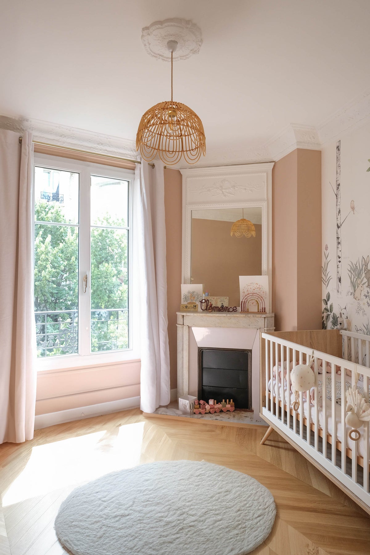 Chambre d'enfant dans un appartement haussmannien parisien, projet Convention par Ombre d'Or : murs rosés, cheminée en marbre, suspension en rotin et papier peint forestier.