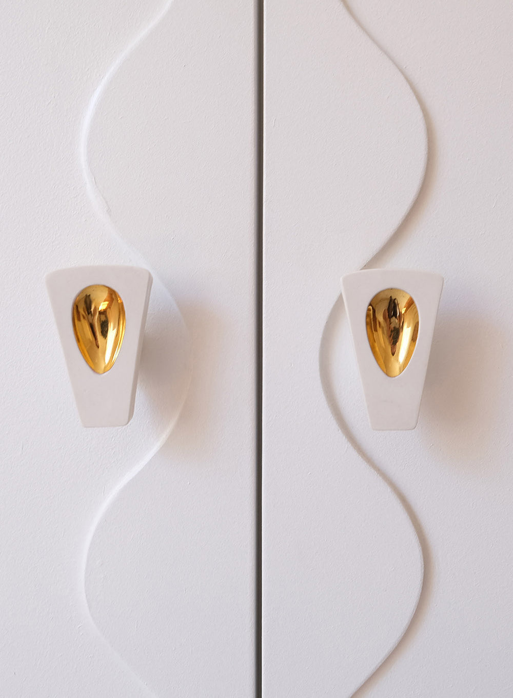 Détail de boutons de meuble dorés intégrés à un dressing sculptural aux lignes ondulées. Céramique d'art sur mesure par Ombre d'Or.