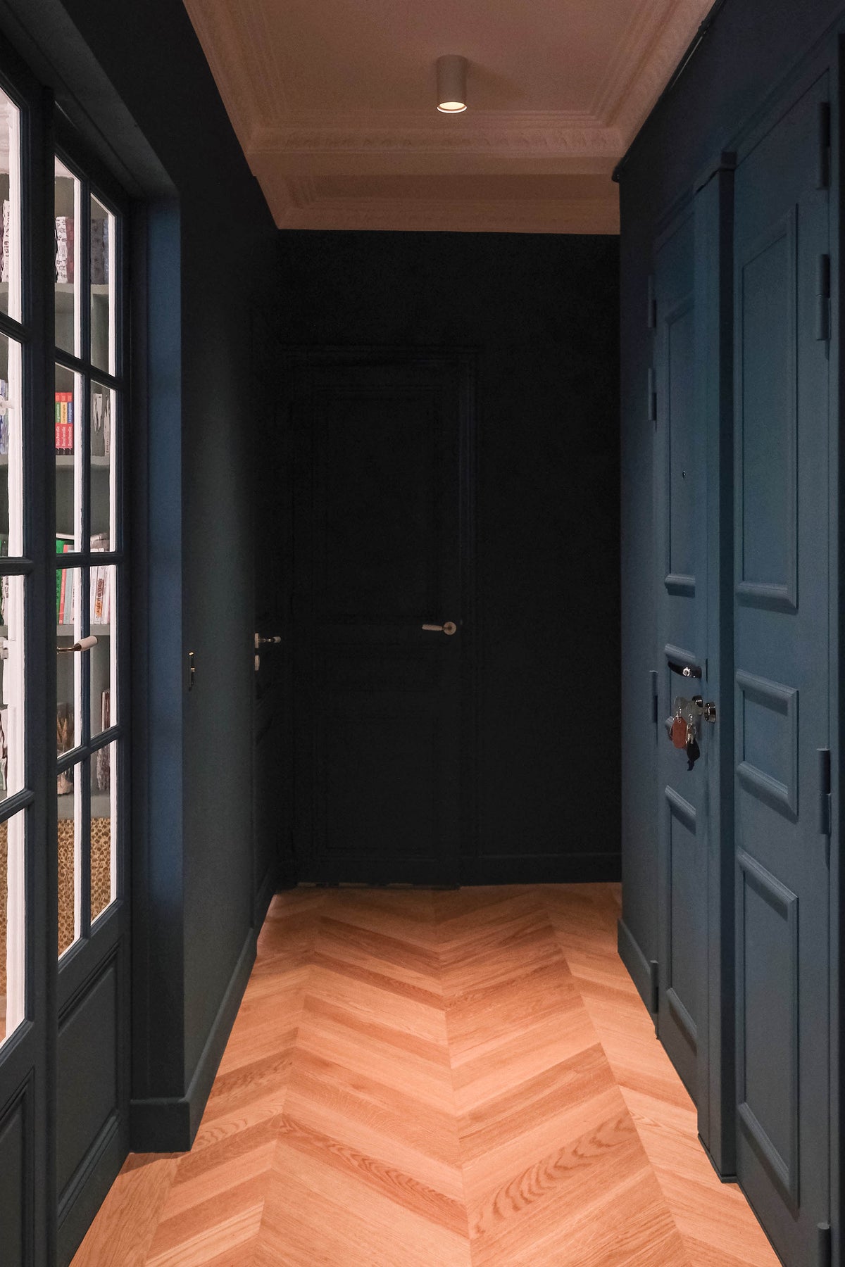 Couloir bleu nuit d'un appartement haussmannien parisien, projet Convention par Ombre d'Or : plafond en bois, parquet point de Hongrie et verrière atelier en perspective.