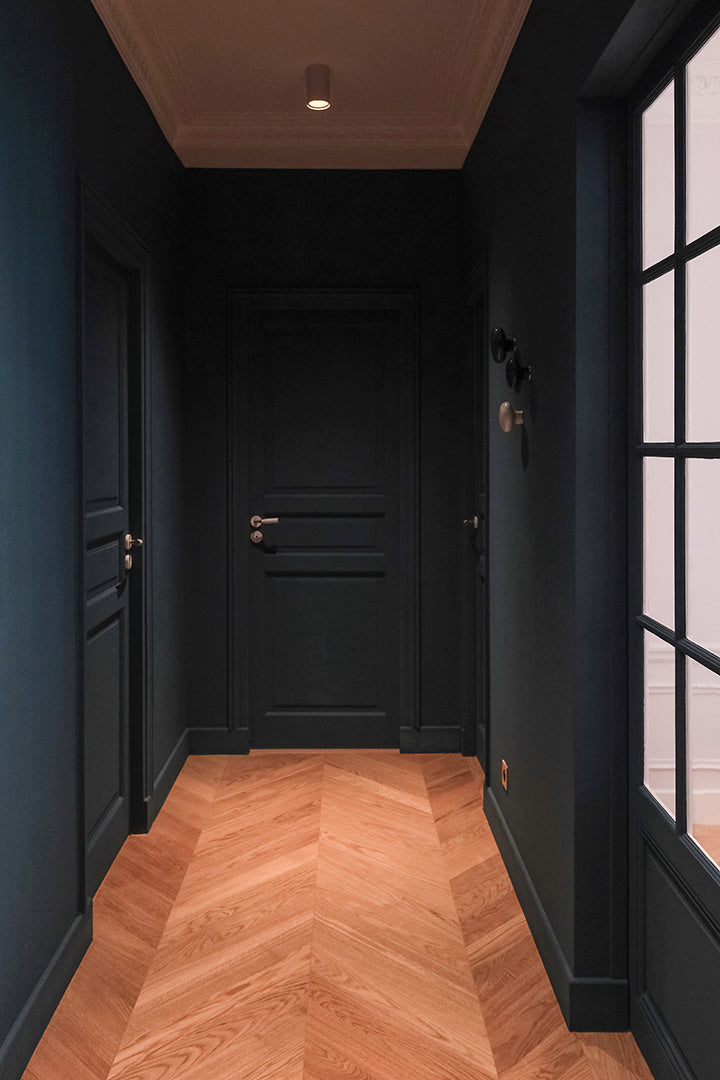 Couloir d'un appartement haussmannien à Paris, projet Convention par Ombre d'Or : murs peints en bleu nuit, plafond en bois de chêne, parquet point de Hongrie et verrière atelier.