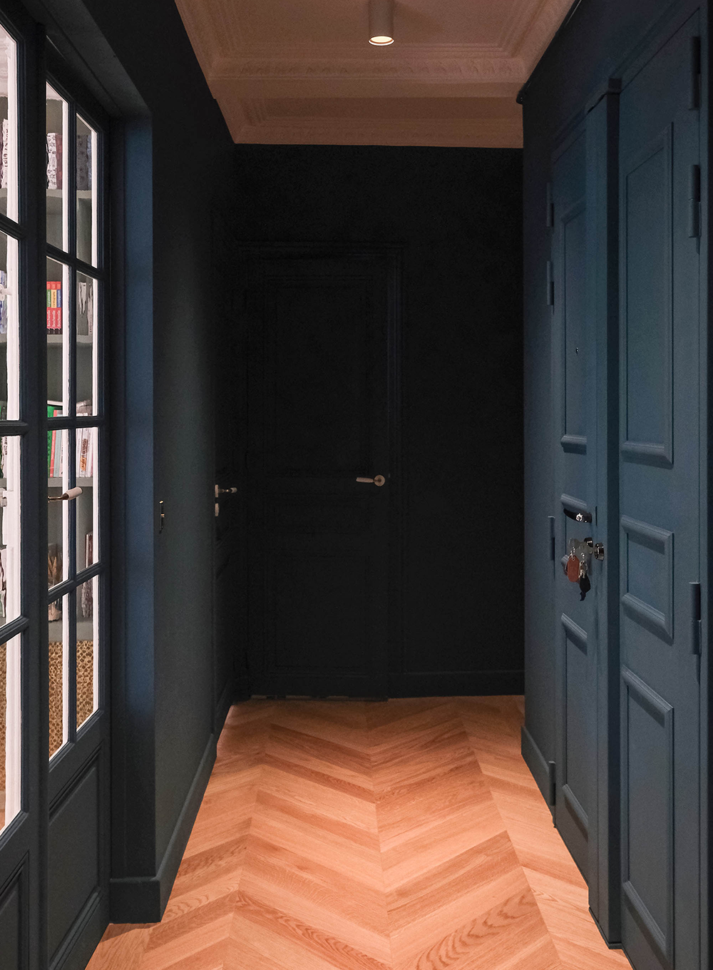 Design d'espace d’un couloir haussmannien à Paris avec parquet chevron, portes moulurées et palette bleu profond.