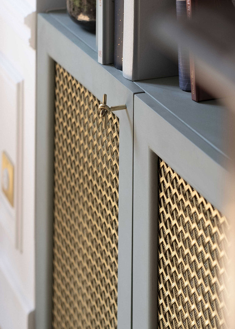 Détail d'un meuble sur-mesure avec portes en cannage de laiton, projet Convention par Ombre d'Or : ébénisterie peinte en vert sauge dans un appartement haussmannien parisien.
