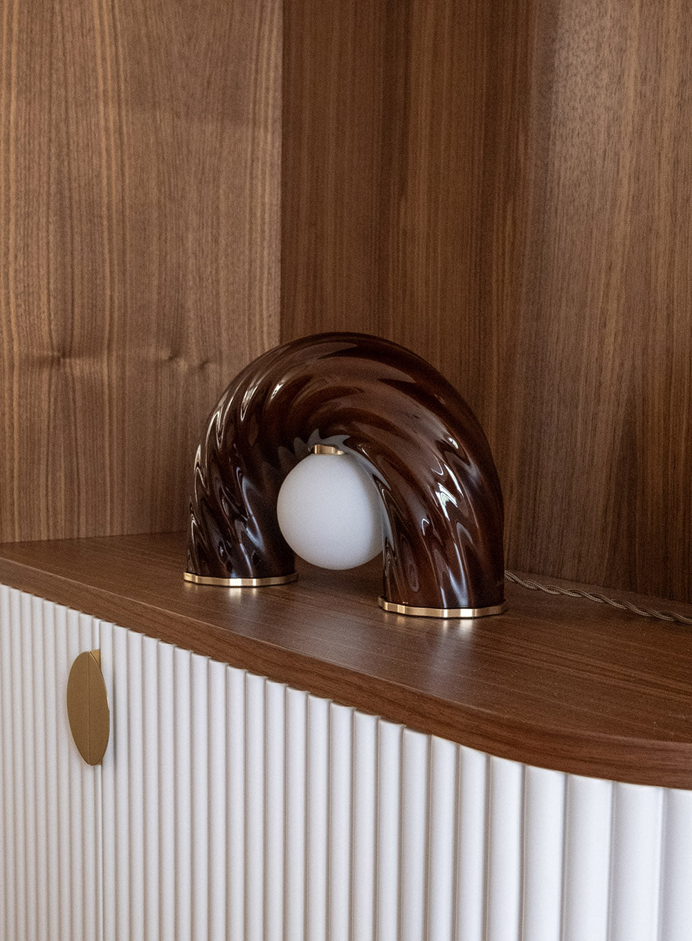 Détail de décoration intérieure au projet de Saint Mandé avec luminaire sculptural en céramique marron et bibliothèque sur mesure aux finitions texturées.