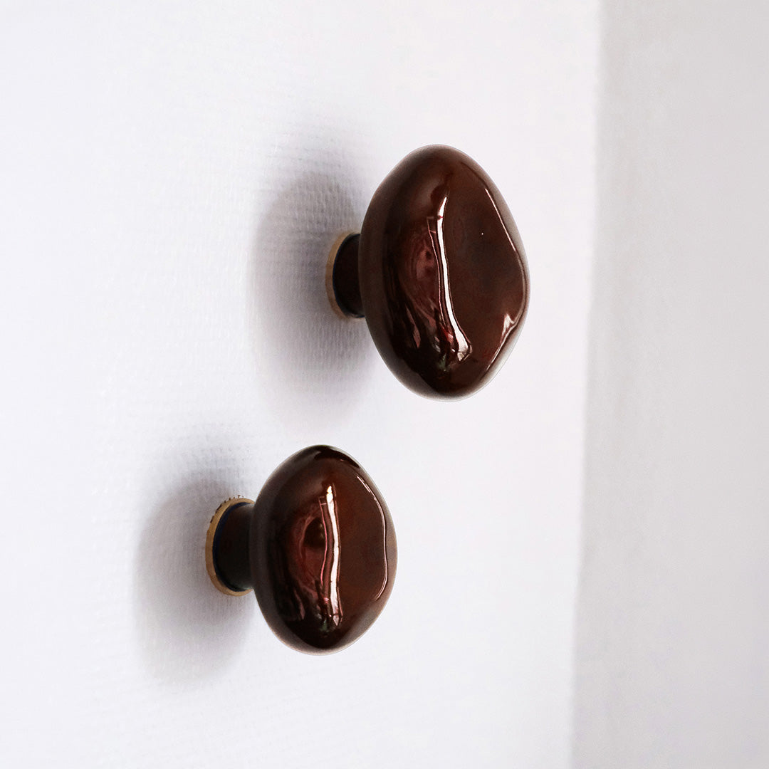 deux patères Agate couleur grenat  en porcelaine émaillée, installées sur un mur blanc vue rapproché #couleur_grenat