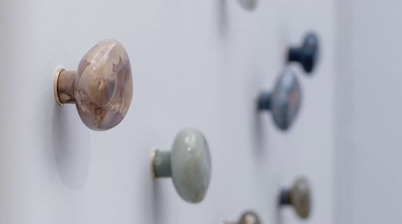 Gros plan en mouvement sur des patères Agate en céramique émaillée et cristallisée, présentées sur un mur clair.