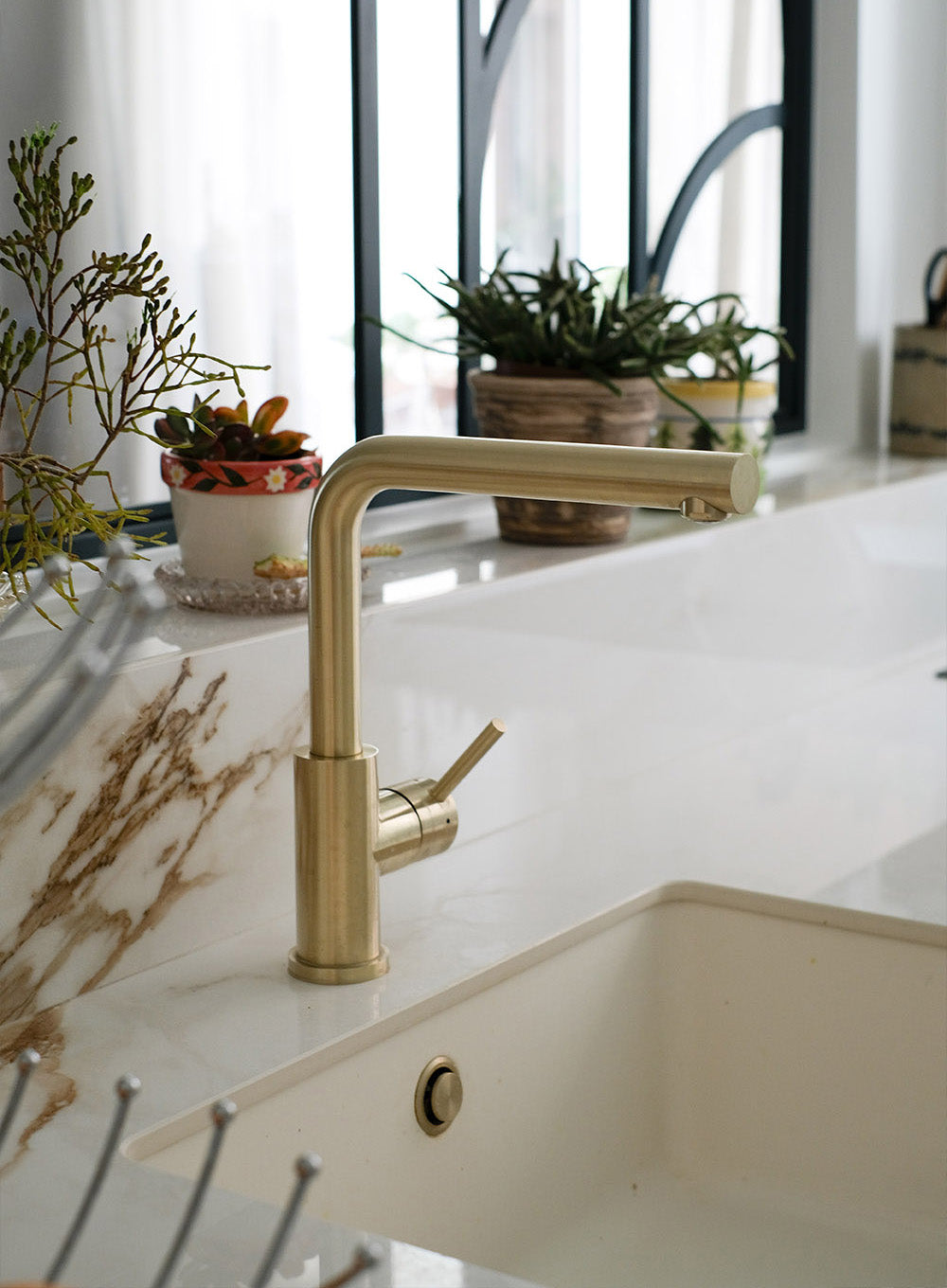 Rénovation d'une cuisine à Saint Mandé. Design d’intérieur sur mesure haut de gamme avec plan de travail effet marbre, robinetterie en laiton doré et verrière artisanale noire.
