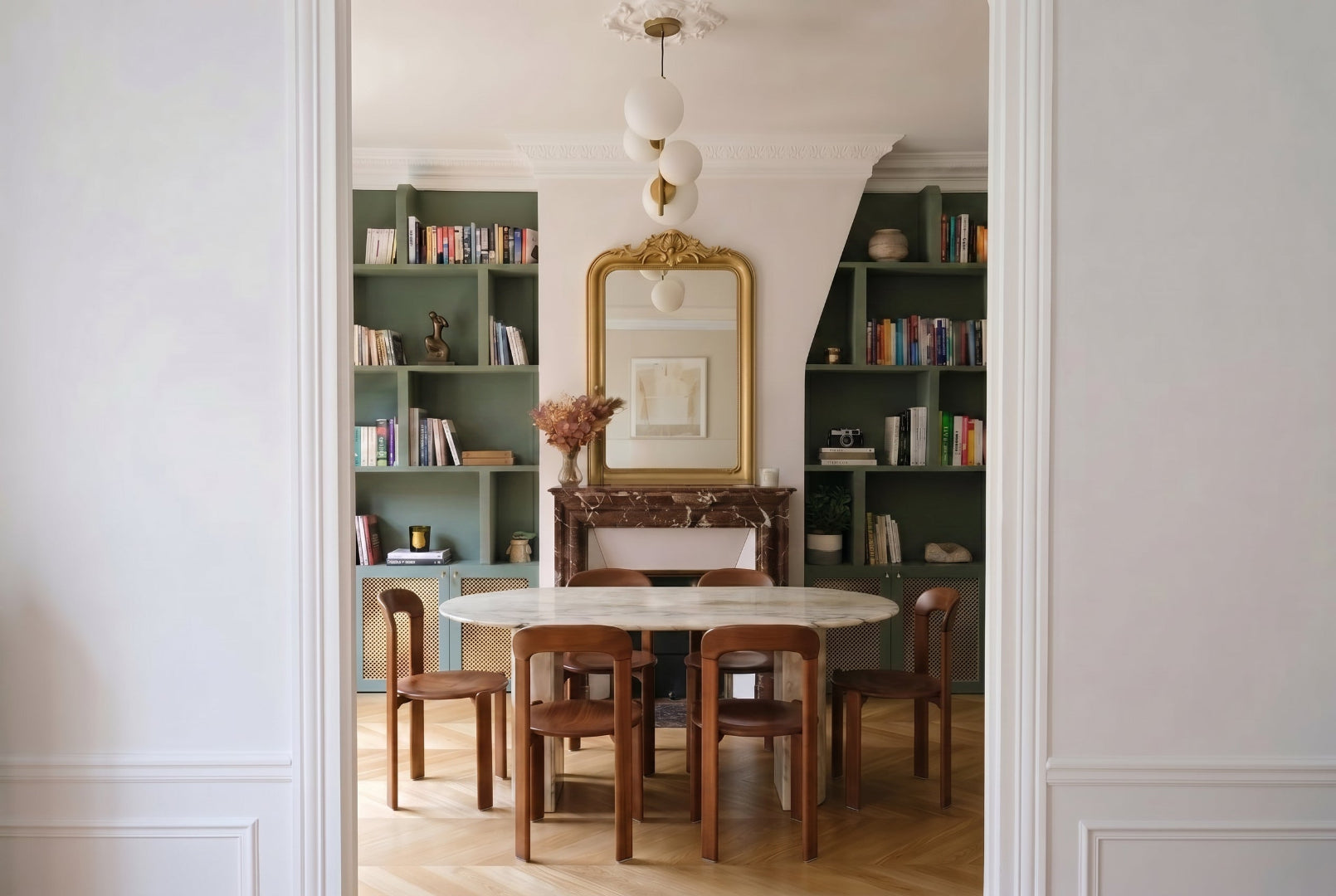 Salle à manger d'un appartement haussmannien à Paris, projet Convention par Ombre d'Or : bibliothèque vert sauge, miroir ancien doré, table ronde en marbre et chaises bois.