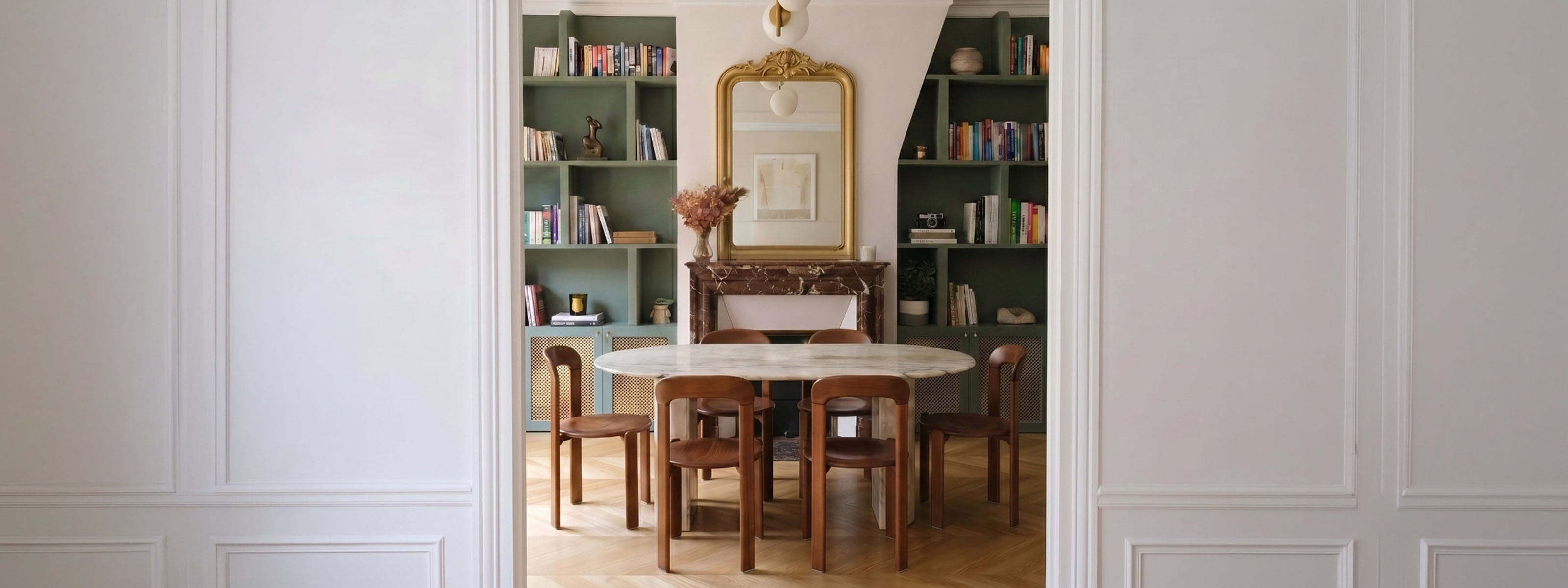 Salle à manger d'un appartement haussmannien à Paris, projet Convention par Ombre d'Or : bibliothèque vert sauge, miroir ancien doré, table ronde en marbre et chaises bois.