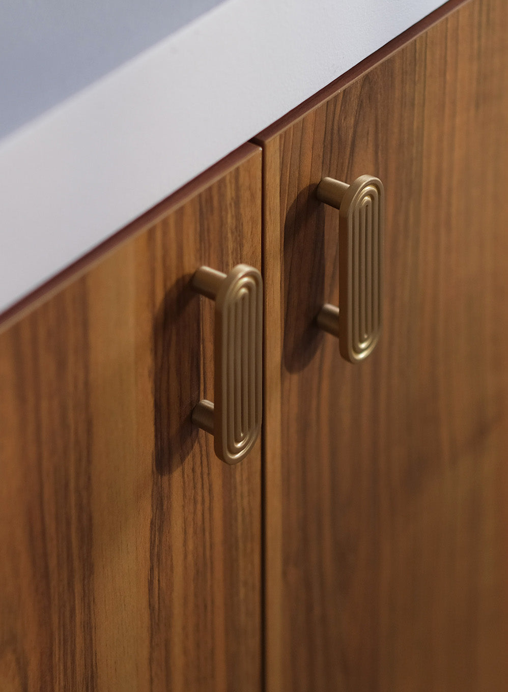 Détail de poignées en laiton doré sur mobilier crée sur mesure en bois foncé dans un projet de design intérieur haut de gamme.