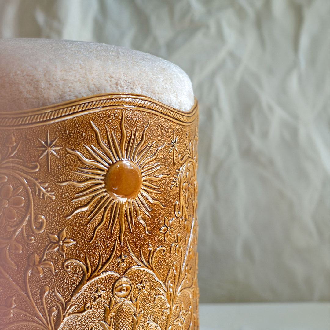 Détail du motif solaire serti d'un cabochon ambré, gravé sur la faïence du tabouret Visconti, sous l'assise en tissu, Ombre d'Or.