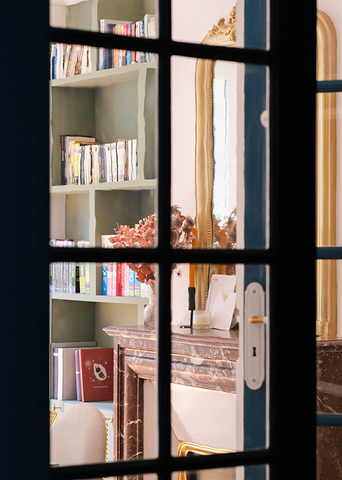 Verrière atelier ouvrant sur la salle à manger du projet Convention par Ombre d'Or : appartement haussmannien parisien avec bibliothèque vert sauge, cheminée en marbre et miroir doré.